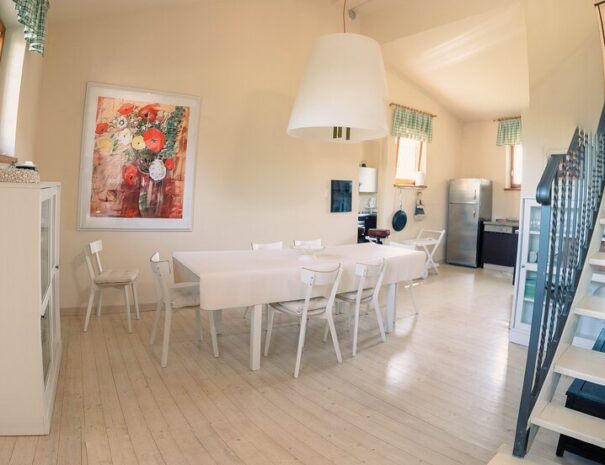 Cucina e sala da pranzo del Loft Verdemare a Fano con arredamento moderno, tavolo ampio, frigorifero in acciaio e scala in ferro battuto – casa vacanze nelle Marche.