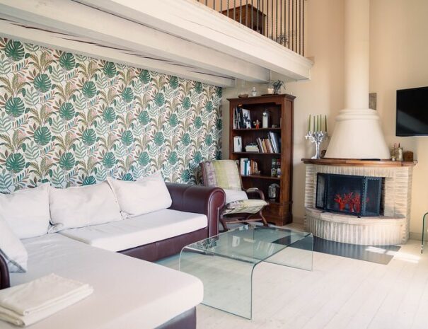 Soggiorno del Loft Verdemare a Fano con camino, parete decorata tropicale, divano angolare e TV – alloggio accogliente per vacanze nelle Marche.